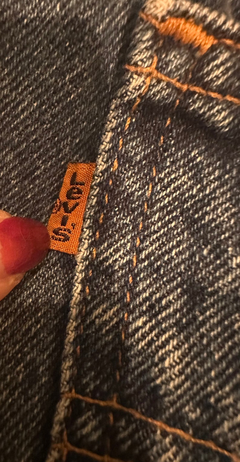 May include: Close-up of a dark blue denim fabric with a brown leather patch that says "Levi's" in white lettering.