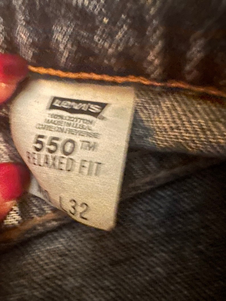 May include: A white Levi's tag with black text. The tag says "100% cotton made in USA care on reverse 550TM Relaxed Fit 32".