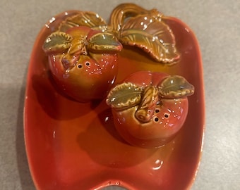 May include: A red ceramic tray with two brown and green ceramic apple salt and pepper shakers.