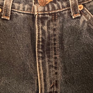 May include: Close-up of the front fly and waistband of a pair of dark blue denim jeans. The jeans have a button fly and belt loops.
