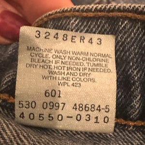 May include: A white care label with black text. The text reads: "3248ER43 MACHINE WASH WARM NORMAL CYCLE, ONLY NON-CHLORINE BLEACH IF NEEDED. TUMBLE DRY HOT, HOT IRON IF NEEDED. WASH AND DRY WITH LIKE COLORS. WPL 423 601 530 0997 48684-5 40550-0310"