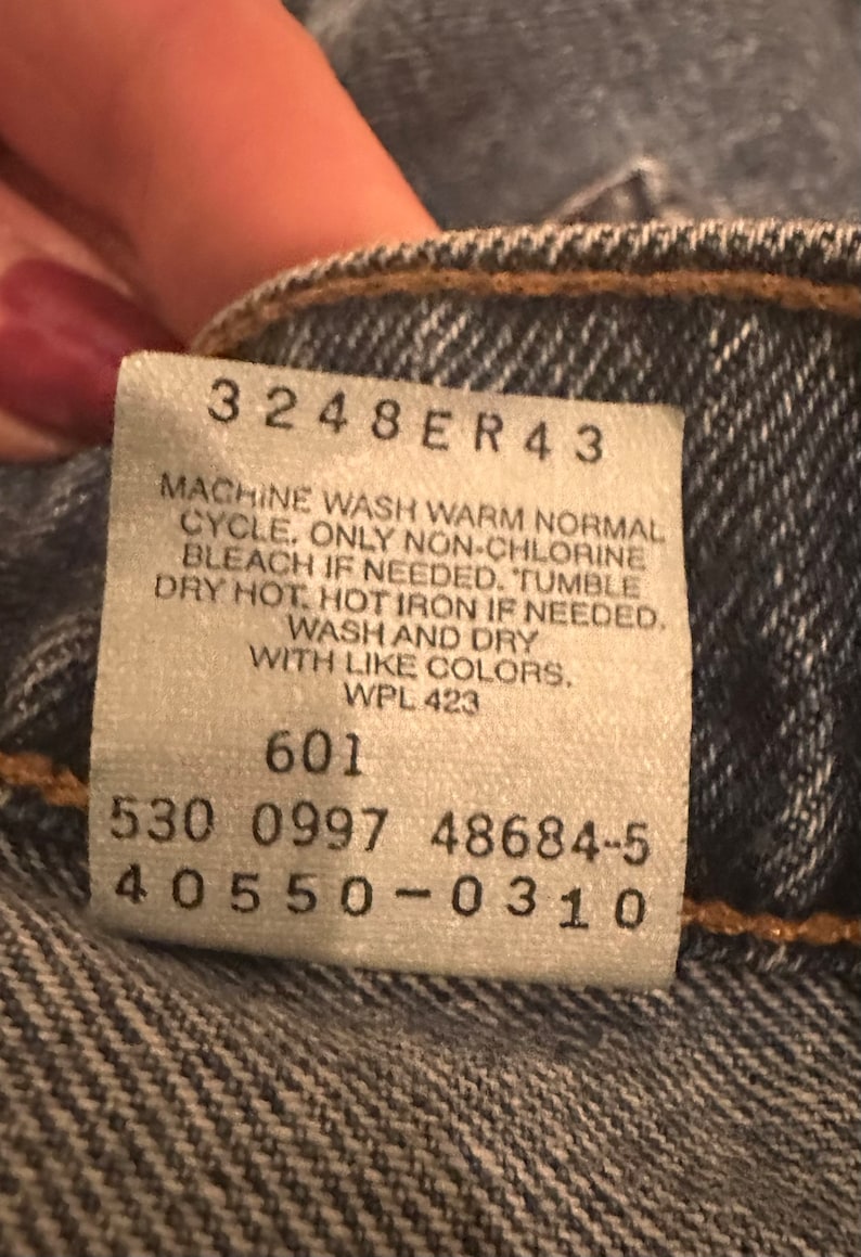 May include: A white care label with black text. The text reads: "3248ER43 MACHINE WASH WARM NORMAL CYCLE, ONLY NON-CHLORINE BLEACH IF NEEDED. TUMBLE DRY HOT, HOT IRON IF NEEDED. WASH AND DRY WITH LIKE COLORS. WPL 423 601 530 0997 48684-5 40550-0310"