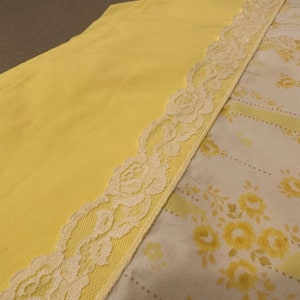 May include: A yellow fabric with a white lace trim. The lace has a floral pattern. The fabric is folded in half, with the lace trim on the outside.