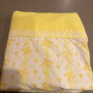 May include: A yellow fitted sheet with a white and yellow floral pattern and a white lace trim.