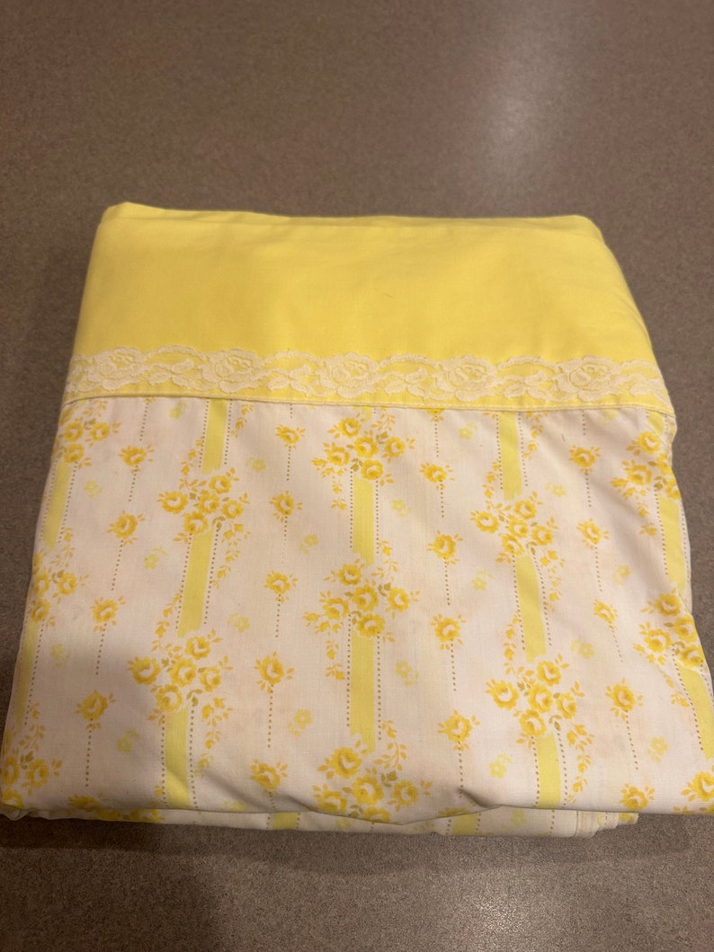 May include: A yellow fitted sheet with a white and yellow floral pattern and a white lace trim.