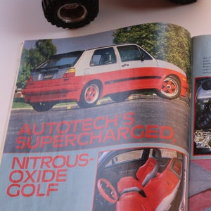 以下が含まれることがあります： スーパーチャージャーと亜酸化窒素システムを搭載した白と赤のフォルクスワーゲンゴルフを紹介する雑誌の特集ページ。記事では、車の性能と改造について説明しています。雑誌のタイトルは「Autotech's Supercharged Nitrous Oxide Golf」です。