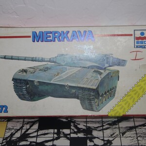 May include: A box for a 1/72 scale model kit of an Israeli Merkava I tank. The box is white with blue and red accents. The tank is depicted in a blue and green camouflage pattern. The box has the text "Merkava I" and "1/72" printed on it.