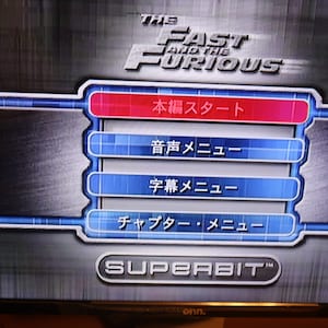 May include: A television screen displaying the main menu for the video game "The Fast and the Furious". The menu options are in Japanese: "Start", "Audio Menu", "Subtitle Menu", "Chapter Menu", and "Superbit".
