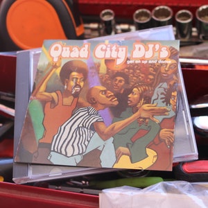 May include: A CD case with a colorful image of a group of people dancing. The text on the case reads "Quad City DJ's get on up and dance".