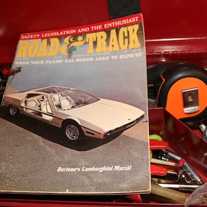 以下が含まれることがあります： 白いランボルギーニ・マルツァルが表紙の、ビンテージのロード＆トラック誌。雑誌の表紙のテキストは「Safety Legislation and the Enthusiast」と「Make Your Plans: All Roads Lead to Expo '67」です。