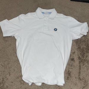 May include: White short-sleeved polo shirt with a blue and white BMW logo on the left chest.