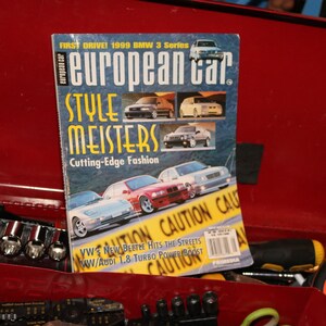 Puede incluir: Una portada de la revista European Car con un BMW Serie 3 rojo de 1999 con el texto "FIRST DRIVE! 1999 BMW 3 Series" y "european car" en letras grandes y en negrita. La portada también presenta una cinta de precaución amarilla con el texto "CAUTION CAUTION CAUTION".