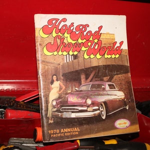 Op de afbeelding: Een vintage tijdschriftcover met een hotrod-auto en een vrouw in een gele jurk. Het tijdschrift is getiteld "Hot Rod Show World" en is de jaarlijkse Pacific-editie van 1978.