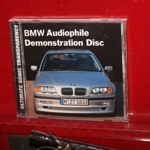 May include: A silver BMW car is featured on the cover of a CD case. The case is labeled "BMW Audiophile Demonstration Disc" and "Ultimate Sonic Transparency".