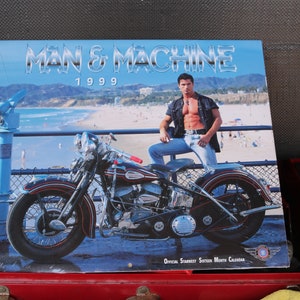 May include: A vintage calendar featuring a black motorcycle with a man sitting on it. The calendar is titled "Man & Machine 1999" and features a beach scene in the background.