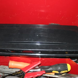 Puede incluir: Una caja de herramientas roja con un contenedor de almacenamiento de plástico negro en su interior. La caja de herramientas está llena de varias herramientas, incluyendo destornilladores, alicates y llaves.