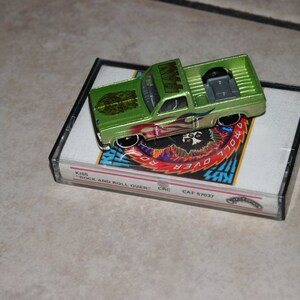 Könnte beinhalten: Ein grüner Spielzeug-LKW mit einem "KISS"-Logo an der Seite, der auf einem Kassetten-Etui liegt. Die Kassette ist "KISS Rock and Roll Over" mit der Katalognummer "CRC CAF 57037".