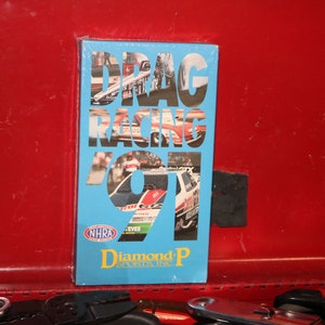 May include: A blue and white VHS tape with the text "DRAG RACING 91" and a logo for NHRA and Diamond P Sports Inc.