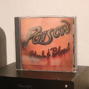 May include: A CD case with a red, white, and black design. The text "Poison Flesh & Blood" is printed on the case.