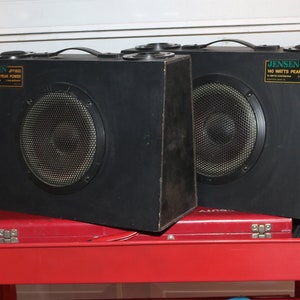 May include: Two black Jensen JPT1002 speakers with a 140 watts peak power rating, sitting on a red metal cart.