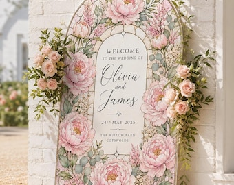 Op de afbeelding: Een boogvormig welkomstbord voor een bruiloft met een rand in glas-in-loodstijl, versierd met roze pioenen en groen blad. De tekst in het midden luidt: WELCOME TO THE WEDDING OF Olivia and James 24TH MAY 2025 THE WILLOW BARN COTSWOLDS.