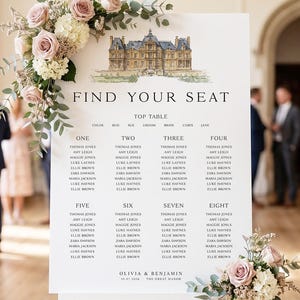 May include: A white wedding seating chart on an easel, adorned with floral arrangements of pink roses and greenery. The chart features a watercolor illustration of a building and the text "FIND YOUR SEAT". Names are listed under table numbers.