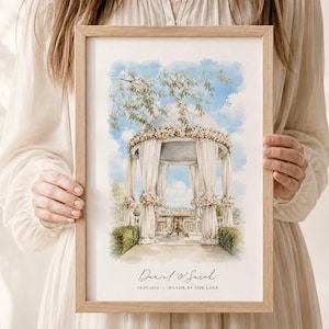 Puede incluir: Una impresi&oacute;n en acuarela enmarcada que muestra un cenador decorado con flores blancas y telas drapeadas bajo un cielo azul. El texto en la parte inferior dice Daniel & Sarah, 18.05.2024, y Manor by the Lake, en un marco de madera clara.