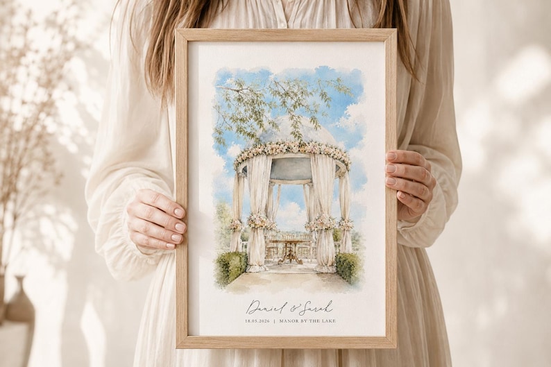 Puede incluir: Una impresi&oacute;n en acuarela enmarcada que muestra un cenador decorado con flores blancas y telas drapeadas bajo un cielo azul. El texto en la parte inferior dice Daniel & Sarah, 18.05.2024, y Manor by the Lake, en un marco de madera clara.