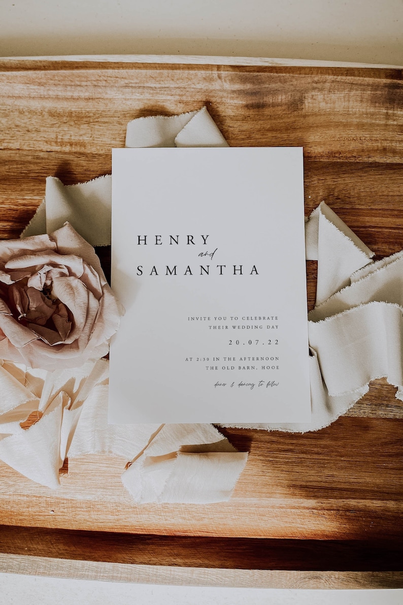Op de afbeelding: Een witte huwelijksuitnodigingskaart met zwarte tekst die de bruiloft van Henry en Samantha aankondigt op 20 juli 2022 om 14:39 uur in The Old Barn, Hooe. De uitnodiging bevat de tekst "faster & dancing to follow".