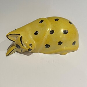 May include: A yellow sleeping cat figurine with black polka dots. The cat is made of soapstone and has a smooth, polished finish.
