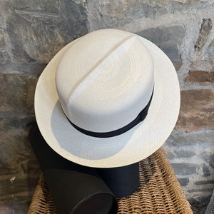 May include: A white Panama hat with a black ribbon band. The hat is sitting on a black and brown cylindrical box.