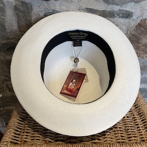 Pu&ograve; includere: Cappello Panama bianco con una fascia nera e un'etichetta che recita "Homero Ortega Genuine Panama Hat Cuenca-Ecuador" e "60".