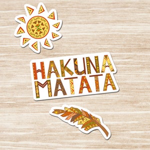 Peut inclure: Trois autocollants colorés avec un motif tribal. Le premier autocollant est un soleil avec des rayons. Le deuxième autocollant dit "Hakuna Matata". Le troisième autocollant est une plume.