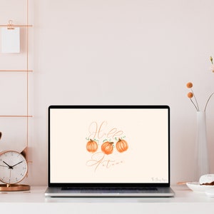 May include: A laptop computer with a light peach background wallpaper featuring the text "Hello Autumn" in a cursive font with three orange pumpkins.