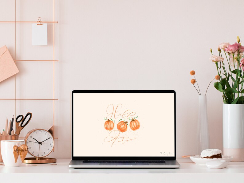 May include: A laptop computer with a light peach background wallpaper featuring the text "Hello Autumn" in a cursive font with three orange pumpkins.