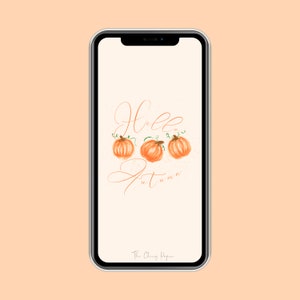 May include: A white phone screen with a digital illustration of three orange pumpkins with green stems and leaves. The text "Hello Autumn" is written in cursive script in brown. The text "The Cheery Paper" is at the bottom of the screen.