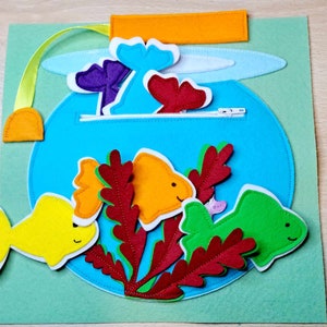 May include: A felt play set with a blue fishbowl, red coral, and yellow, orange, and green fish. The fishbowl has a zipper closure and a felt flap.
