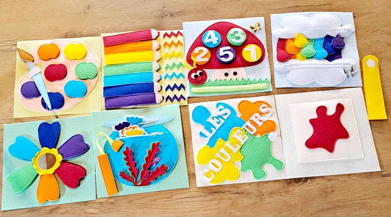 May include: A felt activity book for children with colorful pages featuring a paint palette, rainbow, flower, fishbowl, mushroom with numbers, rainbow in a cloud, and a red paint splatter. The book has the text "Les Couleurs" on one page.