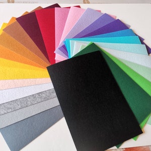 Op de afbeelding: Een waaier van gekleurde vellen vilt in diverse tinten, waaronder rood, roze, geel, groen en blauw. De vellen zijn gerangschikt op een witte ondergrond, met een zwart vel op de voorgrond. Ideaal voor knutselprojecten.