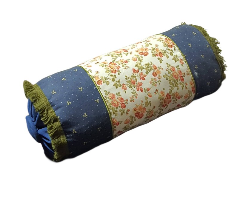 May include: A blue and white floral patterned cylindrical pillow with green fringe trim.