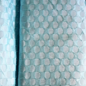 Peut inclure: Un tissu bleu clair avec un motif texturé de cercles blancs. Le tissu a un léger brillant et une texture douce et lisse.