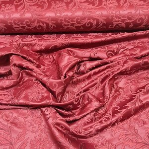 Pode incluir: Tecido vermelho com padrão de damasco. O tecido está dobrado e drapeado, mostrando a textura e o detalhe do design.