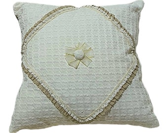 May include: A white pillow with a diamond-shaped design and a beige trim. The pillow has a beige flower-shaped button in the center.