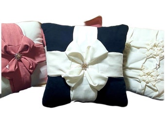 May include: Three decorative throw pillows with a bow design. The pillows are made of a soft, white fabric with black accents. The center pillow has a large white bow with a gold button in the center. The pillows are perfect for adding a touch of elegance to any room.