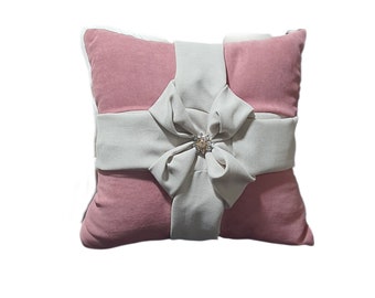 May include: A pink throw pillow with a large white bow and a decorative jeweled accent. The pillow is made of a soft, plush fabric.