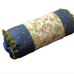 May include: A cylindrical pillow with a blue and white floral pattern. The pillow has a green fringe around the edges.