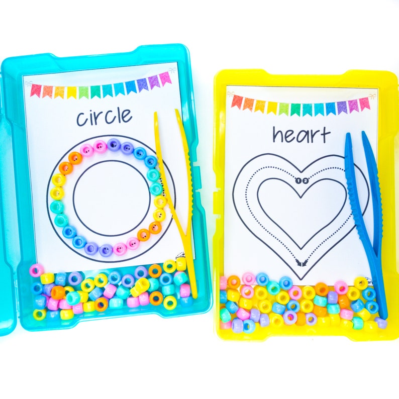 May include: Two colorful plastic containers with lids, each containing a sheet of paper with a shape outline and a set of colorful beads. One container has a circle outline and the word "circle" printed on the paper. The other container has a heart outline and the word "heart" printed on the paper. Both containers have a pair of tweezers.