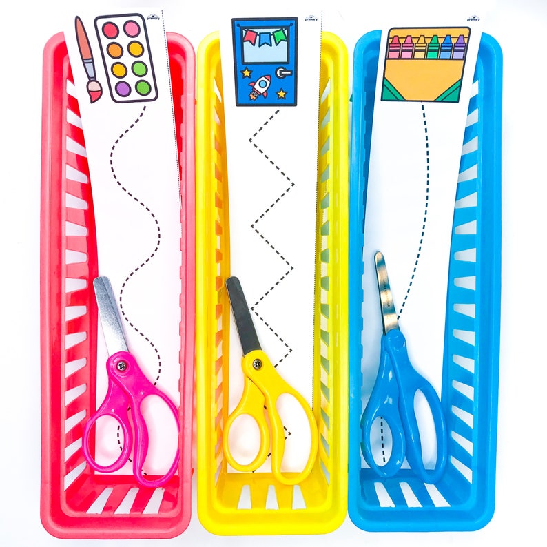 May include: Three colorful plastic storage bins with a wavy, zig-zag, and straight line pattern on white paper inside. Each bin has a pair of child-sized scissors and a picture at the top. The pictures are of a paint palette, a rocket ship, and crayons.