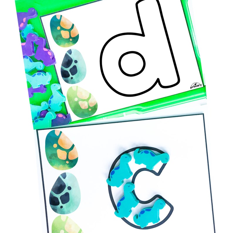 Puede incluir: Dos tarjetas blancas con contornos negros de las letras 'D' y 'C'. La letra 'D' est&aacute; en una tarjeta verde con un borde. La letra 'C' est&aacute; en una tarjeta blanca. Ambas tarjetas tienen huevos de dinosaurio coloridos y figuritas de dinosaurios azules.