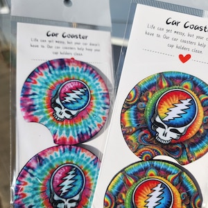 May include: Two sets of car coasters featuring a tie-dye design with a skull and lightning bolt graphic. The text on the card reads "Life can get messy, but your car doesn't have to. Our car coasters help keep your cup holders clean."